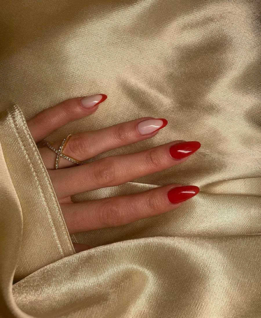 Hand with long red almond nails and a red French tip, resting on gold satin