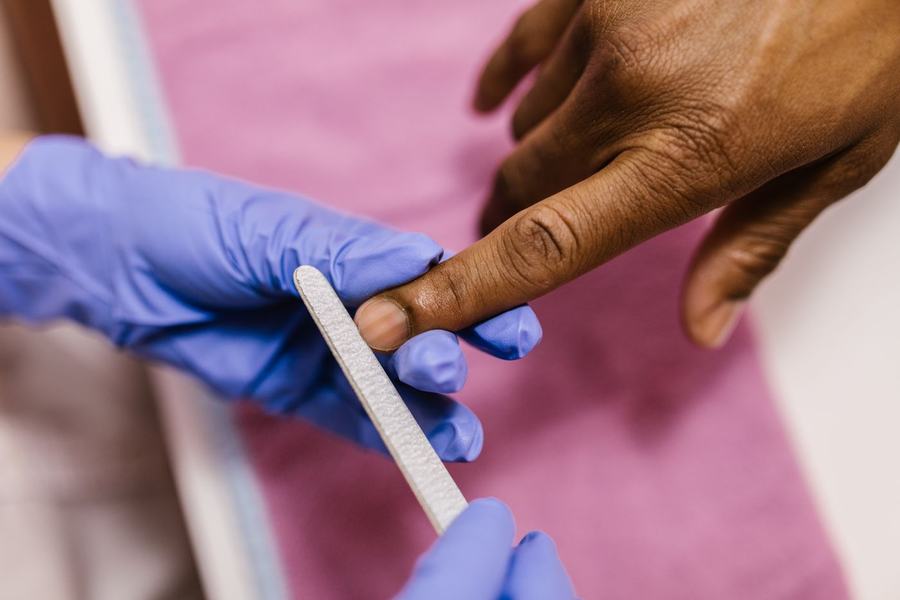 Nail technician in gloves filing a client's nails