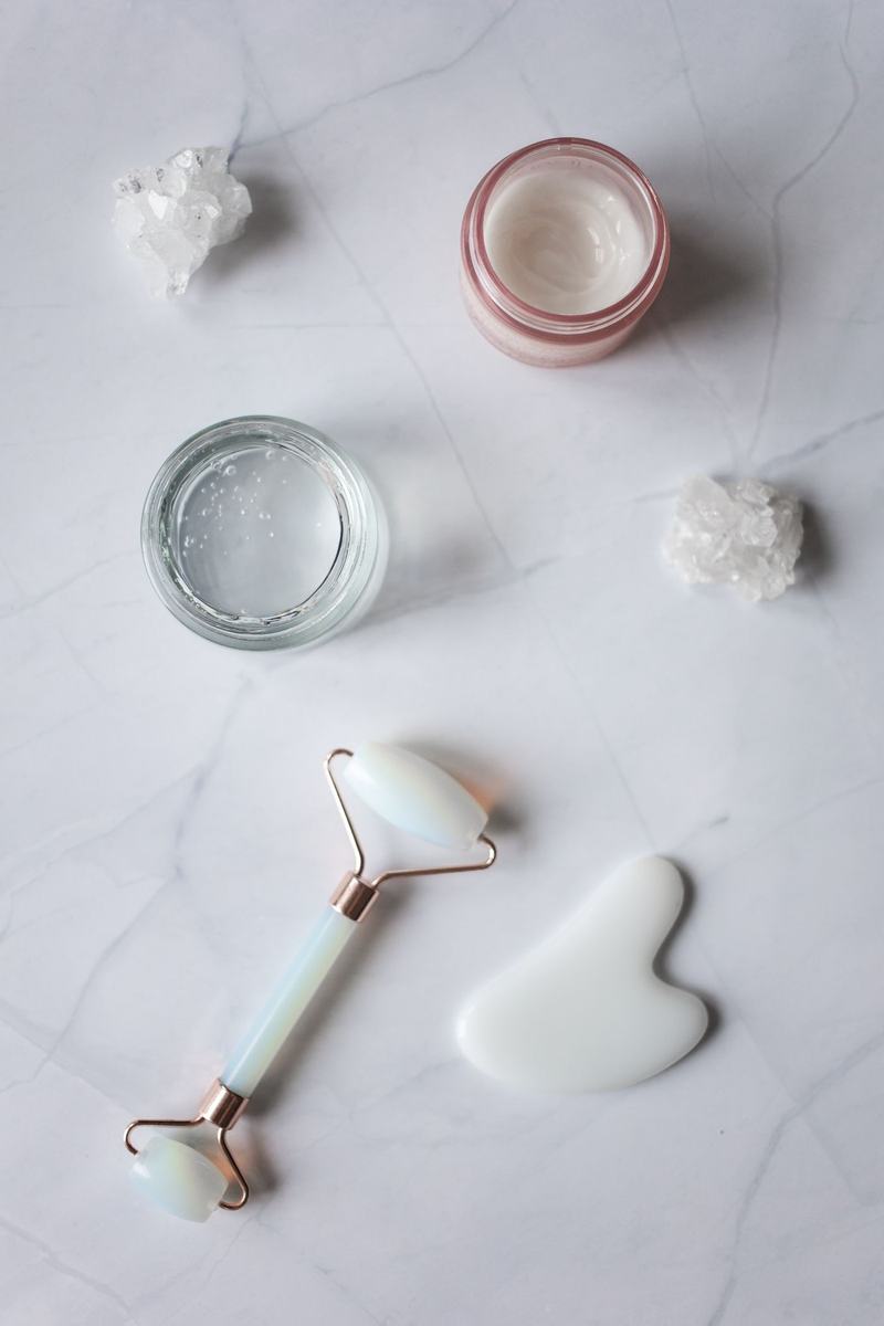 Face cream, jade roller and gua sha stone on white marble